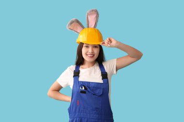 Mavi arka planda tavşan kulaklı Asyalı kadın işçi. Paskalya kutlaması