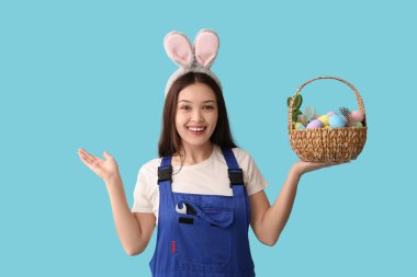 Mavi arka planda Paskalya yumurtaları olan tavşan kulaklı Asyalı kadın işçi.