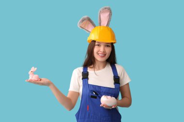 Mavi arka planda Paskalya yumurtaları olan tavşan kulaklı Asyalı kadın işçi.