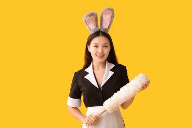 Tavşan kulaklı genç Asyalı oda hizmetçisi ve sarı arka planda toz bezi. Paskalya kutlaması