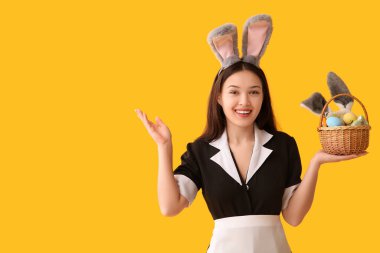 Sarı arka planda Paskalya yumurtaları olan tavşan kulaklı genç Asyalı oda hizmetçisi.