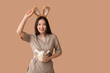 Tavşan kulaklı Asyalı kadın masaj terapisti ve kahverengi arka planda banyo malzemeleri. Paskalya kutlaması