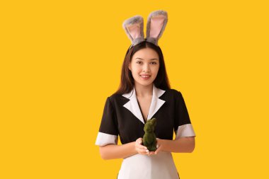 Tavşan kulaklı genç Asyalı oda hizmetçisi ve sarı arka planda Paskalya tavşanı.