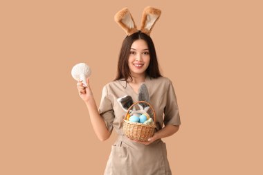 Tavşan kulaklı kadın Asyalı masaj terapisti. Bitkisel çanta ve kahverengi arka planda Paskalya yumurtası.