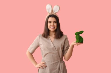 Pembe arka planda Paskalya tavşanı olan tavşan kulaklı kadın masaj terapisti.