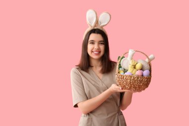 Paskalya yumurtaları ve pembe arka planda bitki torbalarıyla tavşan kulaklı kadın masaj terapisti.
