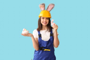 Tavşan kulaklı kadın işçi, paskalya tavşanı ve mavi arka planda yumurtalar.