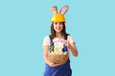Mavi arka planda Paskalya yumurtaları olan tavşan kulaklı kadın işçi.