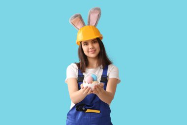 Mavi arka planda Paskalya yumurtaları olan tavşan kulaklı kadın işçi.