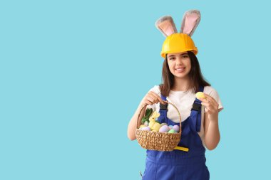 Mavi arka planda Paskalya yumurtaları olan tavşan kulaklı kadın işçi.