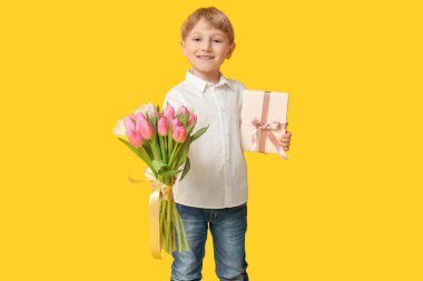 Güzel lalelerle dolu buketi ve sarı arka planda hediye kutusu olan sevimli küçük bir çocuk. Uluslararası Kadınlar Günü