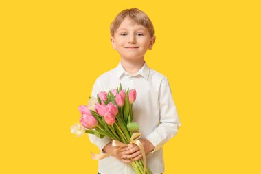 Sarı arka planda bir buket güzel lalesi olan sevimli küçük bir çocuk. Uluslararası Kadınlar Günü