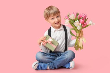 Güzel lalelerle dolu buketi ve pembe arka planda hediye kutusu olan sevimli küçük bir çocuk. Uluslararası Kadınlar Günü
