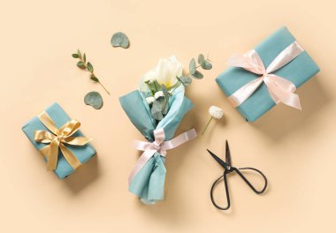 Okaliptüs, makas ve bej arka planda hediye kutularıyla ambalaj kağıdına sarılmış küçük bir buket güzel bahar çiçeği. Uluslararası Kadınlar Günü