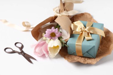 Makas ve beyaz arka planda hediye kutusuyla ambalaj kağıdına sarılmış küçük bir buket güzel bahar çiçeği. Uluslararası Kadınlar Günü