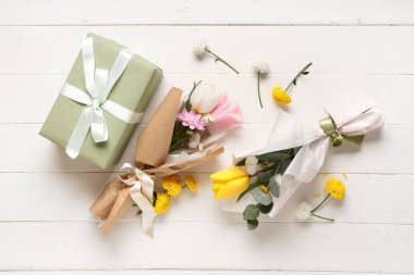 Beyaz ahşap arka planda hediye kutusuyla ambalaj kağıdına sarılmış güzel bahar çiçeklerinden oluşan mini buketler. Uluslararası Kadınlar Günü