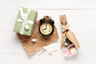 Hediye kutusu ve beyaz ahşap arka planda çalar saati olan ambalaj kağıdına sarılı küçük bir buket güzel bahar çiçeği. Uluslararası Kadınlar Günü