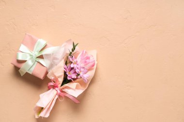 Bej arka planda hediye kutusuyla ambalaj kağıdına sarılmış küçük bir buket güzel bahar çiçeği. Uluslararası Kadınlar Günü