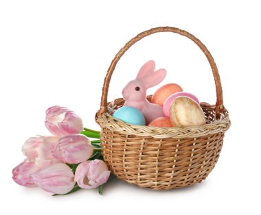 Beyaz arka planda boyanmış Paskalya yumurtaları, tavşan ve pembe laleler olan sepet.