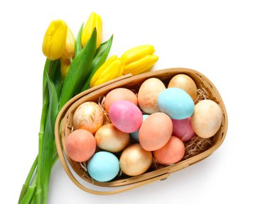 Güzel Paskalya yumurtaları ve beyaz arka planda sarı laleler olan sepet.