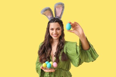 Sarı arka planda boyanmış Paskalya yumurtaları olan tavşan kulaklı güzel bir kadın.