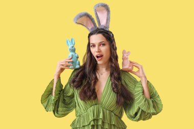 Sarı arka planda Paskalya tavşanları olan tavşan kulaklı güzel bir kadın.