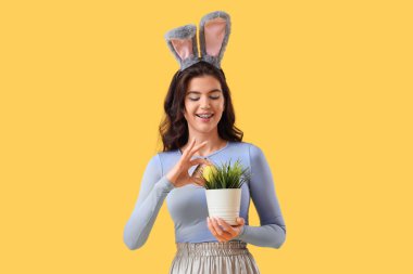 Tavşan kulaklı genç bir kadın. Paskalya yumurtaları ve sarı arka planda yeşil çimenler.