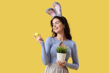 Tavşan kulaklı genç bir kadın. Paskalya yumurtaları ve sarı arka planda yeşil çimenler.