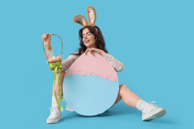 Büyük kağıt kulaklı, güzel bir kadın. Mavi arka planda Paskalya yumurtası ve sepeti.