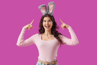 Güzel bir kadın mor arka plandaki tavşan kulaklarını işaret ediyor. Paskalya kutlaması