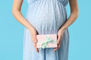 Mavi arka planda hediye kutusu olan genç hamile bir kadın. Uluslararası Kadınlar Günü
