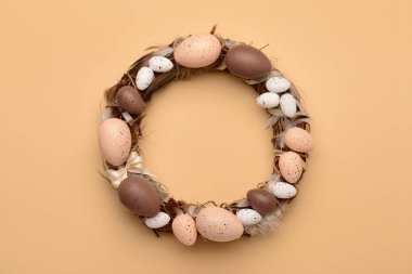 Bej arka planda yumurta ve tüylerden yapılmış Paskalya çelengi.