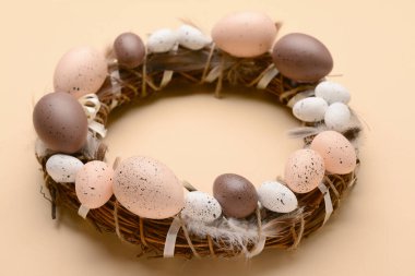 Bej arka planda yumurta ve tüylerden yapılmış Paskalya çelengi.