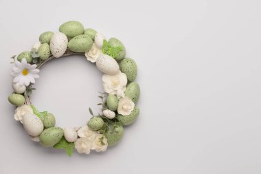 Beyaz çiçeklerden yapılmış Paskalya çelengi, yeşil boyalı yumurta ve açık arkaplanda kelebekler.