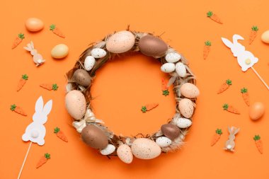 Turuncu arka planda yumurta ve tüylerden yapılmış Paskalya çelengi.