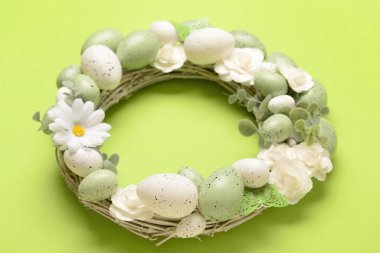 Beyaz çiçekli Paskalya çelengi, parlak yeşil arka planda yumurtalar ve kelebekler.