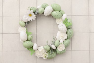 Beyaz fayans üzerinde çiçekler, yumurtalar ve kelebeklerden oluşan Paskalya çelengi.