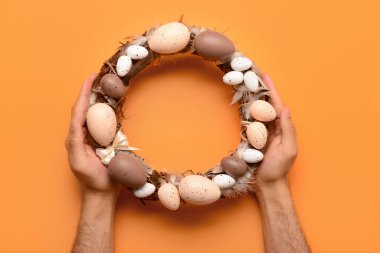 Turuncu arka planda Paskalya çelengi tutan erkek.