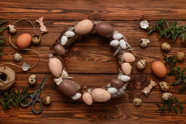 Ahşap arka planda yumurta ve tüylerle süslenmiş Paskalya çelengi. Üst görünüm