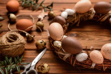 Ahşap arka planda yumurta ve tüylerle süslenmiş Paskalya çelengi.