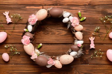 Ahşap arka planda yumurta ve çiçeklerle süslenmiş şık bir Paskalya çelengi. Üst görünüm