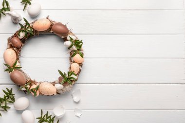 Beyaz ahşap masada yumurta ve çiçeklerle süslenmiş güzel Paskalya çelengi. Üst görünüm