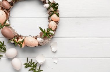 Beyaz ahşap masada yumurta ve çiçeklerle süslenmiş güzel Paskalya çelengi. Üst görünüm