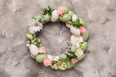 Gri arka planda yumurta ve çiçeklerle süslenmiş şık bir Paskalya çelengi. Üst görünüm