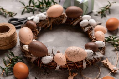 Paskalya çelengi, gri arka planda yumurta ve tüylerle süslenmiş.