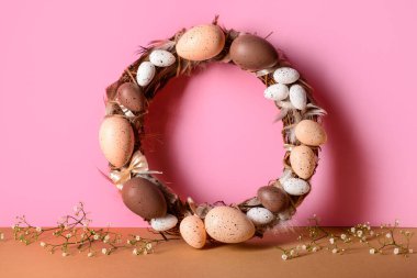 Paskalya çelengi, pembe duvarın yanındaki masada yumurta ve tüylerle süslenmiş.