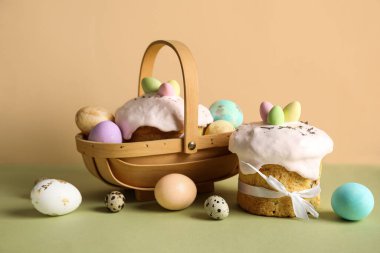 Hediye sepetli kompozisyon, lezzetli paskalya pastaları ve renkli arka planda boyanmış yumurtalar.