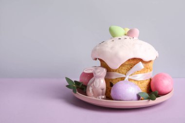 Lezzetli Paskalya pastası, porselen tavşan ve renkli arka planda tabakta boyanmış yumurtalar.