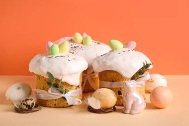 Lezzetli Paskalya pastaları, porselen tavşanlar ve renkli arka planda boyanmış yumurtalar.