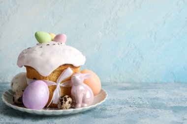 Lezzetli dekore edilmiş Paskalya pastası, porselen tavşan ve renkli arka planda tabakta boyanmış yumurtalar.